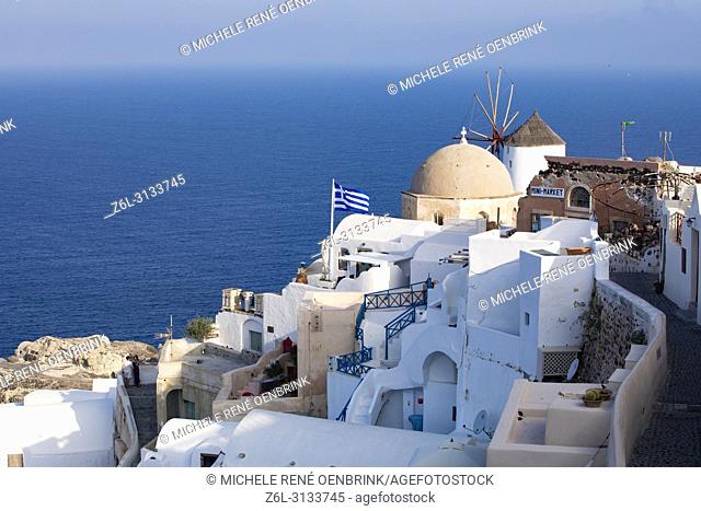 Traditional Greek flag with domed Orthodox Church overlooking the Aegean Sea in Oia Santorini Greece