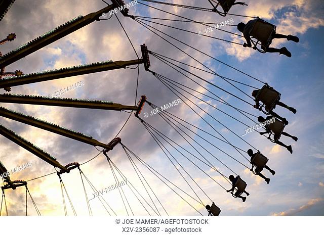 An amusement ride at a county fair sends riders soaring through the air at sunset