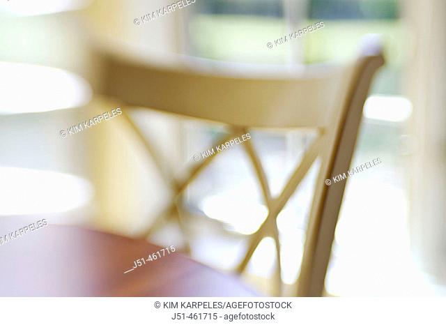 White wooden chair at wooden table, window behind in eating area, abstract view with selective focus and blur