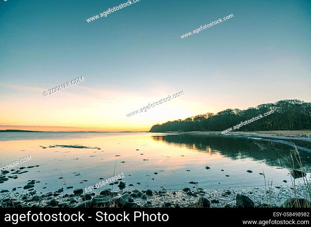 Lake in the sunrise with rocks on the beach and a forest by the shore