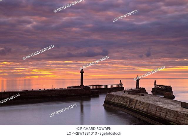 England, North Yorkshire, Whitby. Sunset over the West and East piers at Whitby on a summers evening