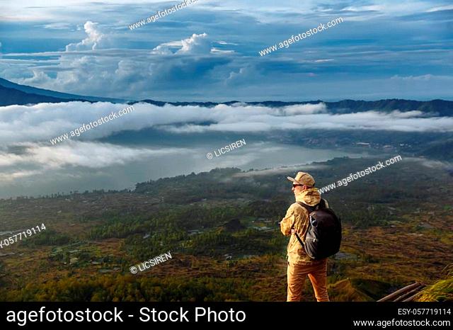 Man tourist looks at the sunrise on the volcano Batur on the island of Blai in Indonesia. Hiker man with backpack travel on top volcano