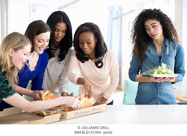 Woman with salad watching friends eat pizza