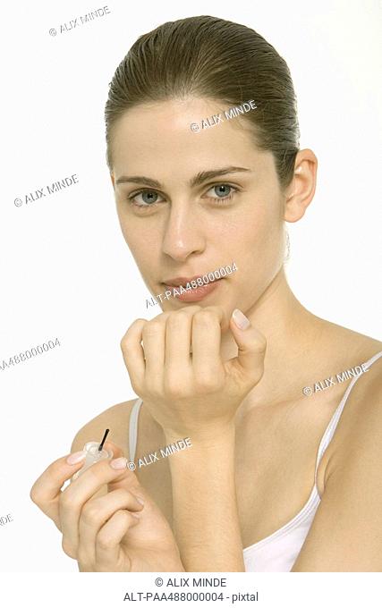 Woman blowing on wet nail polish, head and shoulders, looking at camera