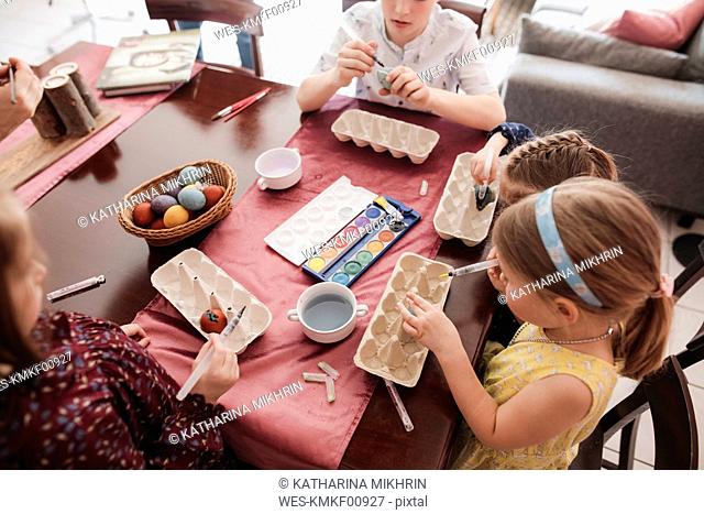 Children painting Easter eggs on table at home