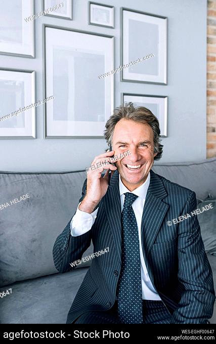 Happy mature businessman talking on mobile phone at home