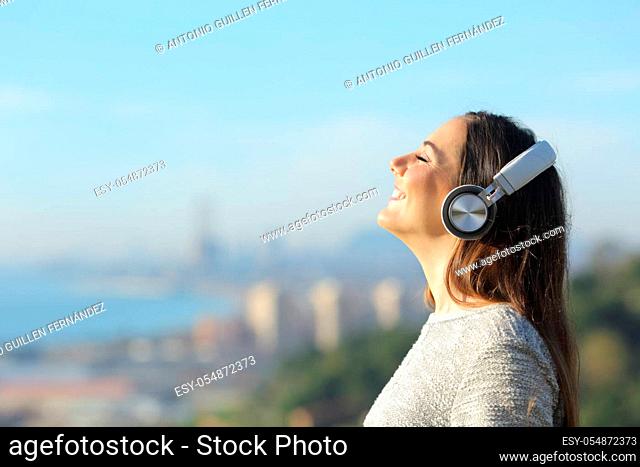 Happy girl smiling and breathing using headphones while enjoying the sun light outdoors