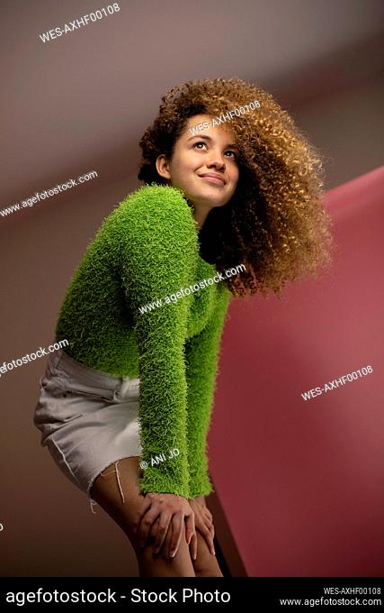 Smiling young woman looking away while bending with hands on knees at studio