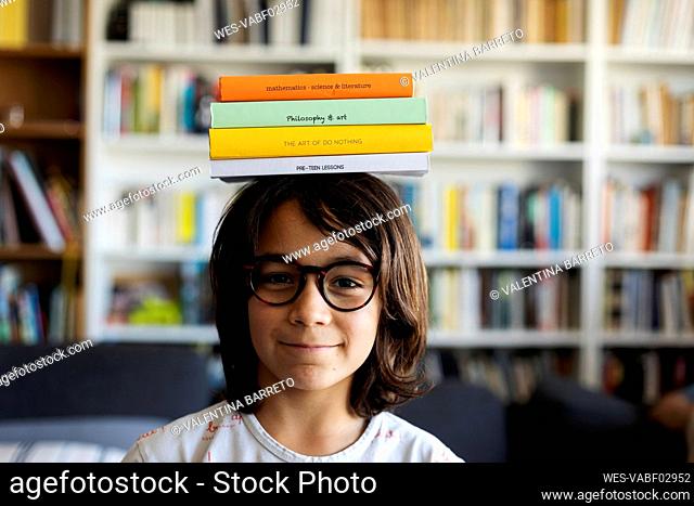 Portrait of smiling boy balancing stack of books on his head