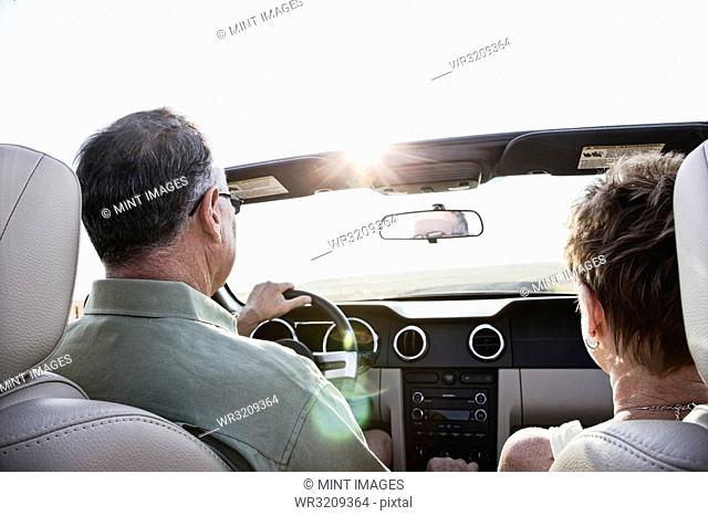 View from behind of senior couple in a convertible sports car driving on a highway at sunset in eastern Washington State, USA