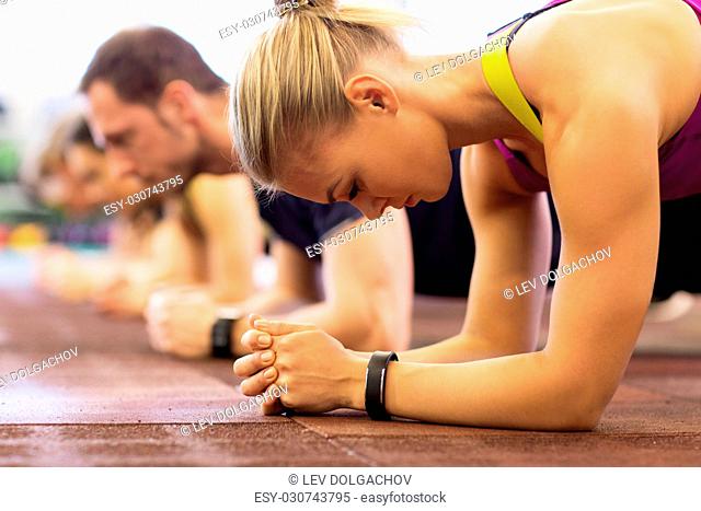fitness, sport, exercising, people and healthy lifestyle concept - close up of woman with heart-rate tracker at group training doing plank exercise in gym