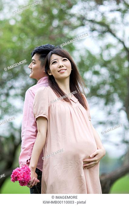 Pregnant woman and young man standing with back to back and holding flowers with smile