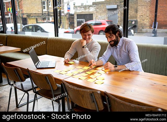Smiling businessmen discussing over adhesive note while sitting at desk in coworking office