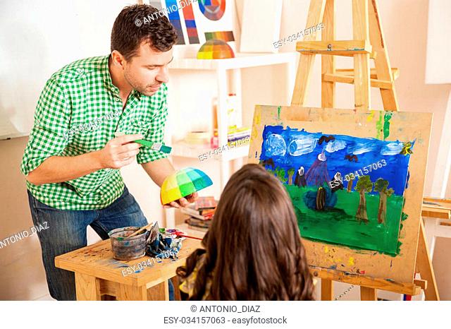 Handsome young art teacher talking about colors with a little girl during class