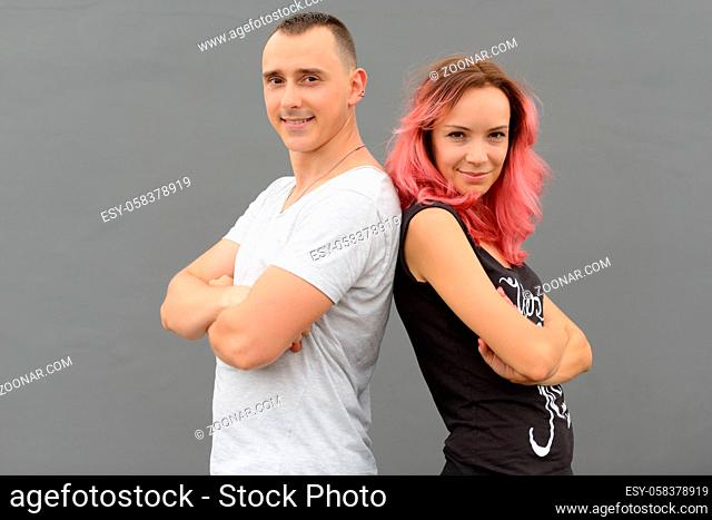 Portrait of handsome man and beautiful woman with pink hair as couple together and in love against gray wall outdoors