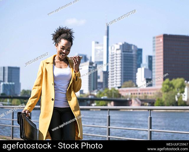Smiling businesswoman sending voicemail through mobile phone on sunny day