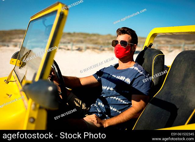 Caucasian man wearing face mask and sunglasses sitting in beach buggy