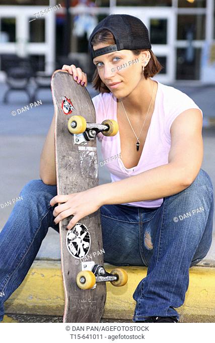 Girl with a skateboard sitting on the sidewalk