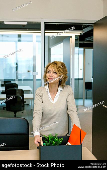 Businesswoman with box looking away while standing at desk in office
