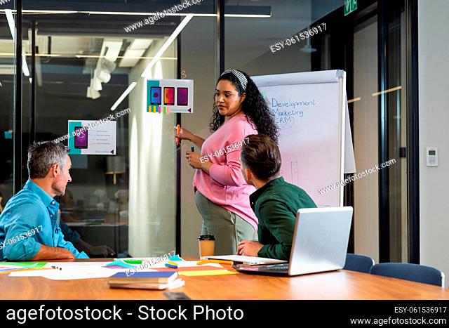 Young biracial businesswoman explaining strategy to colleagues over flipchart in meeting at office