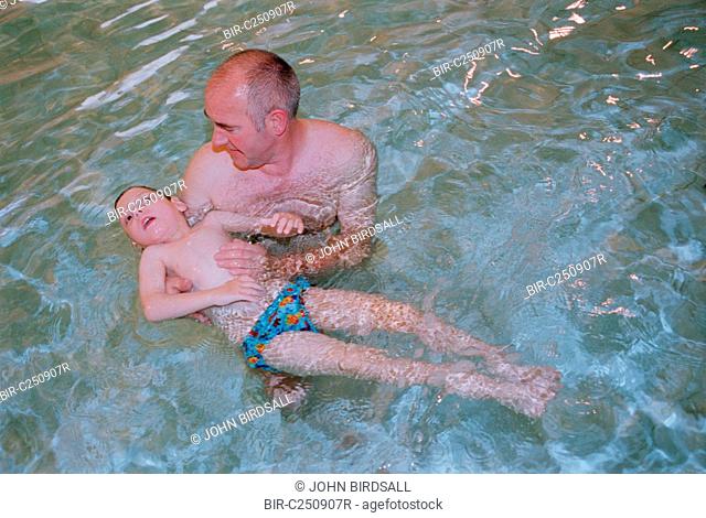 Father supporting young son with severe Cerebral Palsy, cortical blindness, epilepsy and severe developmental delay in public swimming pool