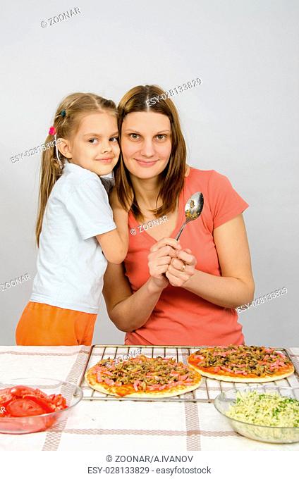 Daughter hugging her mother six years, which is preparing a pizza
