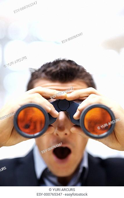 Portrait of a surprised young business man looking through binoculars