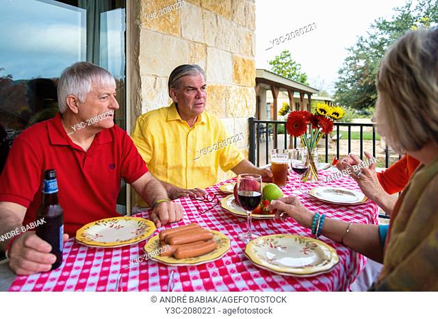 Two retired couples at a backyard barbecue party. Caucasian ethnicity, around 60 years old. Food and drinks, like fresh fruit, sausages, beer and wine