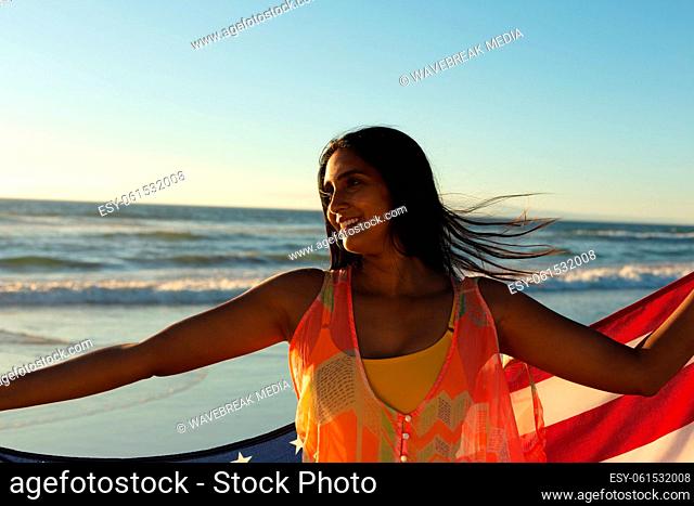 Mixed race patriotic woman on the beach holding american flag