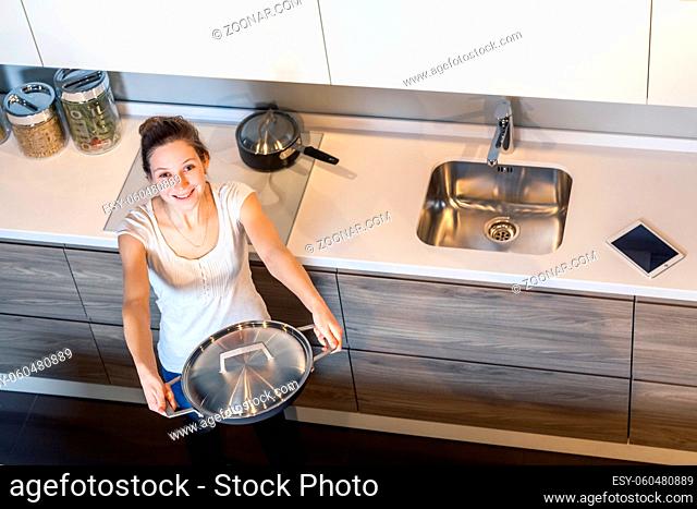 Happy beautiful woman with toothy smile holding kitchen pan and sharing. looking at camera. top view