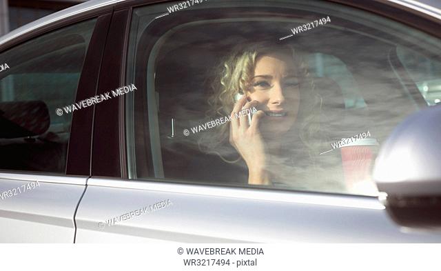 Female executive with coffee cup talking on mobile phone in a car