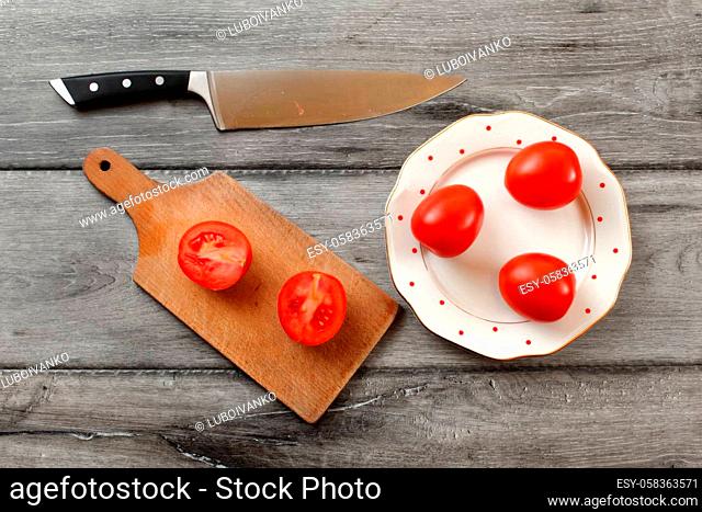Table top view on three tomatoes on white porcelain plate with red dots, cutting board with tomato cut to half next to it