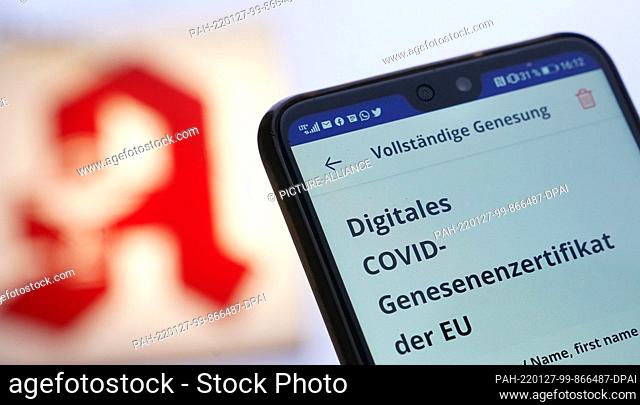 26 January 2022, ---: ILLUSTRATION - A man holds up his smartphone with a digital Covid recovery certificate in front of a pharmacy logo