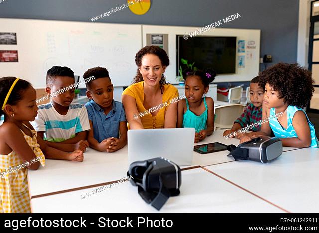 Caucasian young female teacher showing laptop to african american elementary students in class