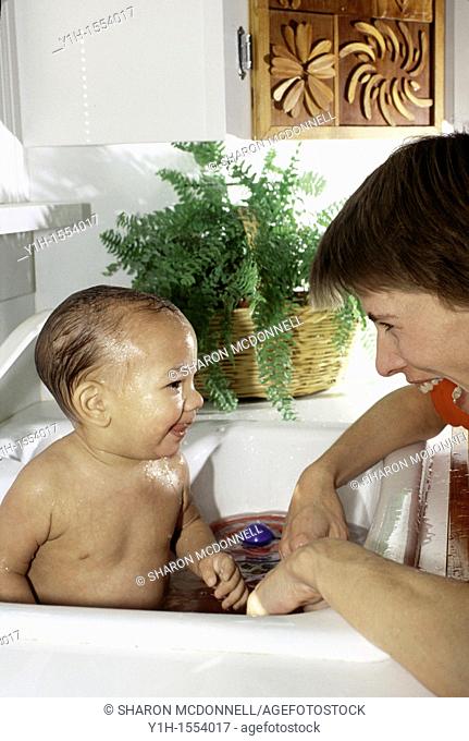 Mother and infant boy share a smile and moment of bonding during a sink bath
