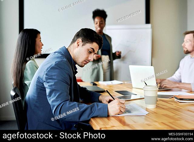 Young businessman making notes sitting at desk in meeting at office