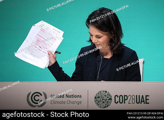 13 December 2023, United Arab Emirates, Dubai: Annalena Baerbock (Alliance 90/The Greens), Federal Foreign Minister, holds up papers at a press conference