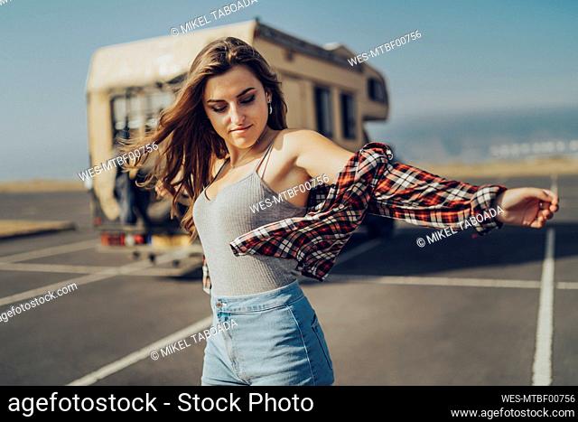 Carefree woman standing with arms outstretched on road