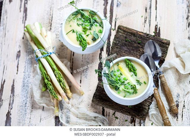 Cream of white asparagus soup garnished with white and green asparagus spears, pea shots and chives