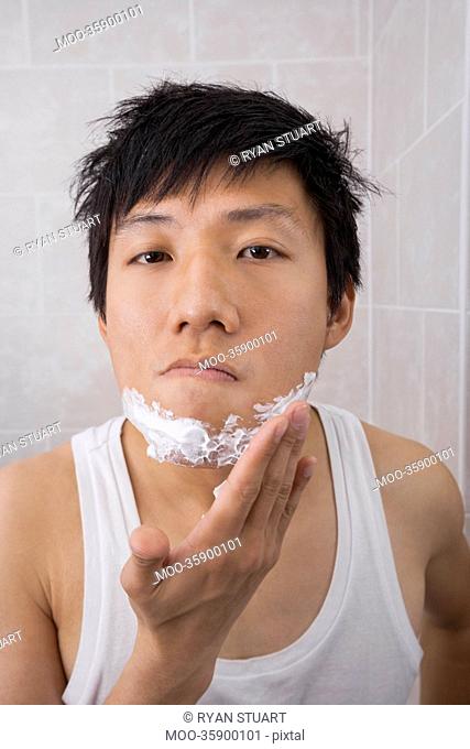 Portrait of mid adult man applying shaving foam on face in bathroom
