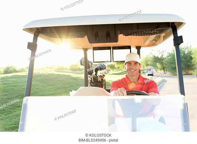 Portrait of Hispanic golfer driving golf cart