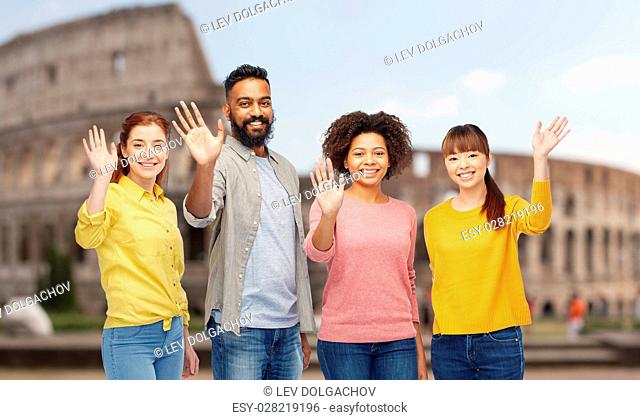 travel, tourism, diversity and people concept - international group of happy smiling men and women waving hands over coliseum background