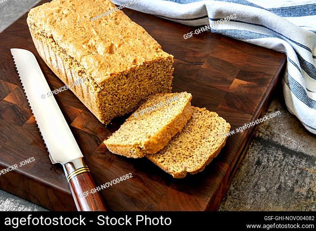 Loaf of almond bread with two slices on wood cutting board with bread knife