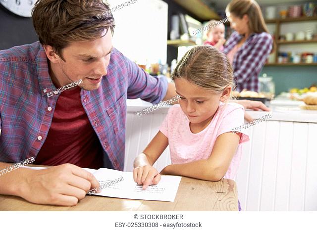 Father Reading Book With Daughter At Kitchen Table