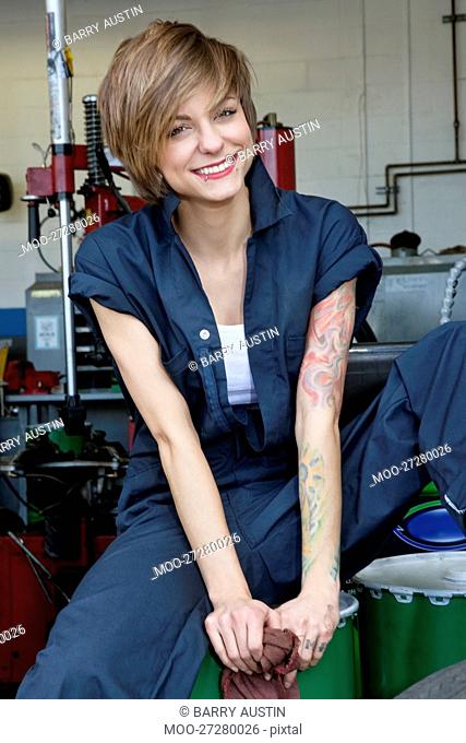 Portrait of a happy young female mechanic sitting on oil drum in car workshop