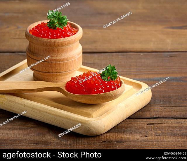 red caviar of pink salmon lies in a wooden spoon on a cutting board. Brown wooden table