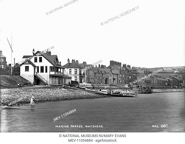 Marine Parade, Whitehead - a view across the sea to the boathouse with boats on the slipway and the promenade and houses behind