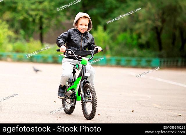 portrait of adorable little urban boy wearing black leather jacket. City style. Urban kids. The boy learns to ride a bike. Child driving a bicycle