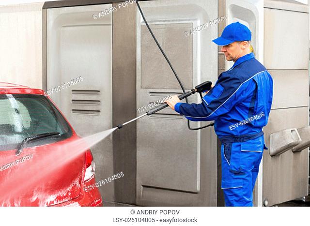 Mature serviceman with high pressure water jet washing red car at service station