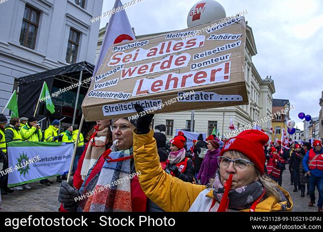 28 November 2023, Mecklenburg-Western Pomerania, Schwerin: A teacher holds a sign reading ""Be everything, become a teacher!"" during a protest in the ongoing...